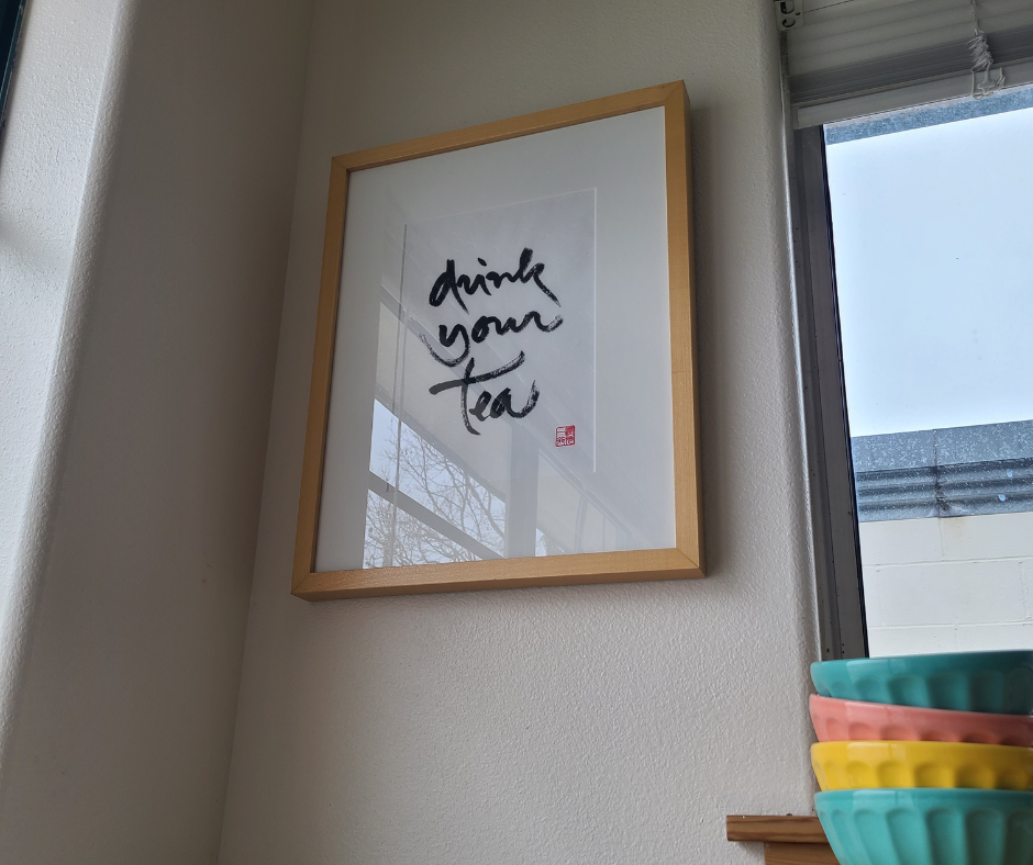 Photo of a framed calligraphy print that says "drink your tea" 